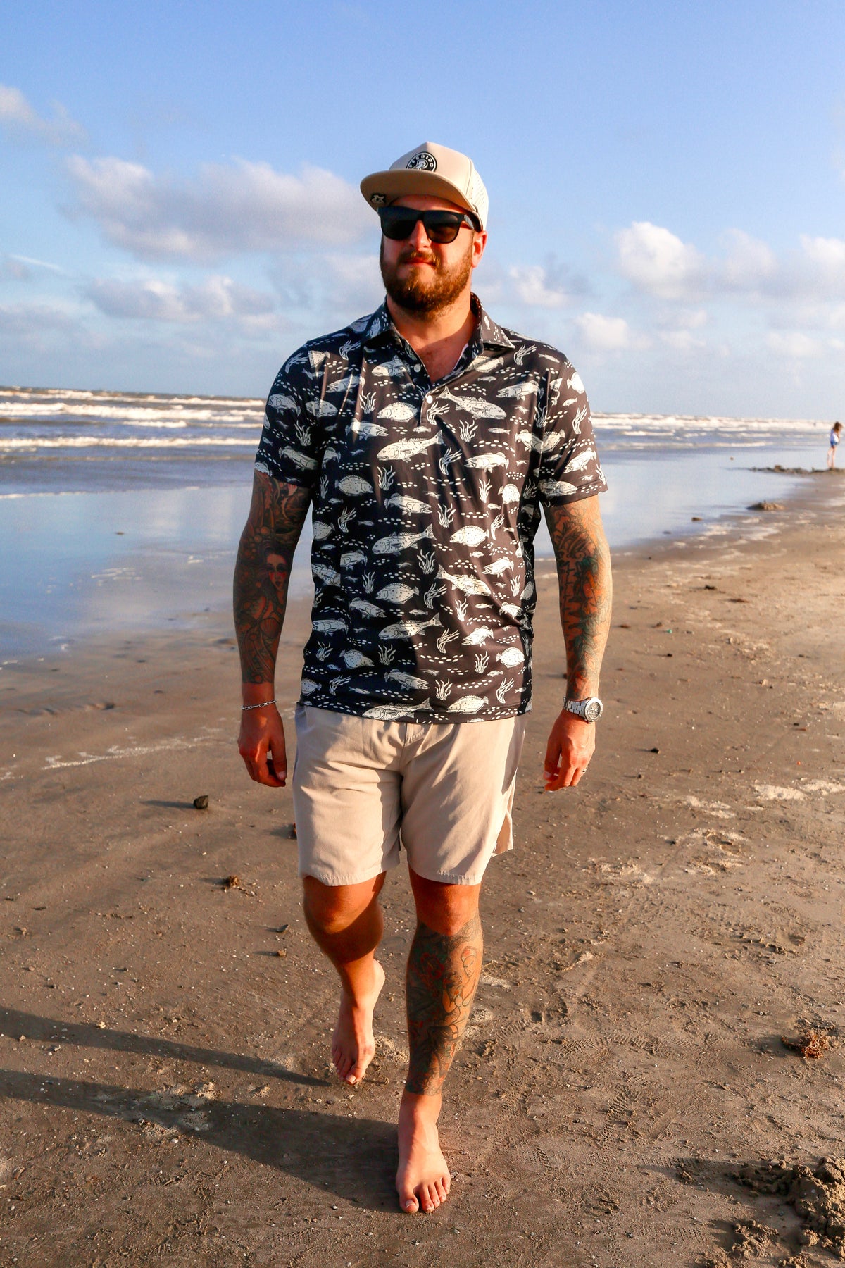 Full-body shot of man walking along shoreline wearing black Texas Slam polo.