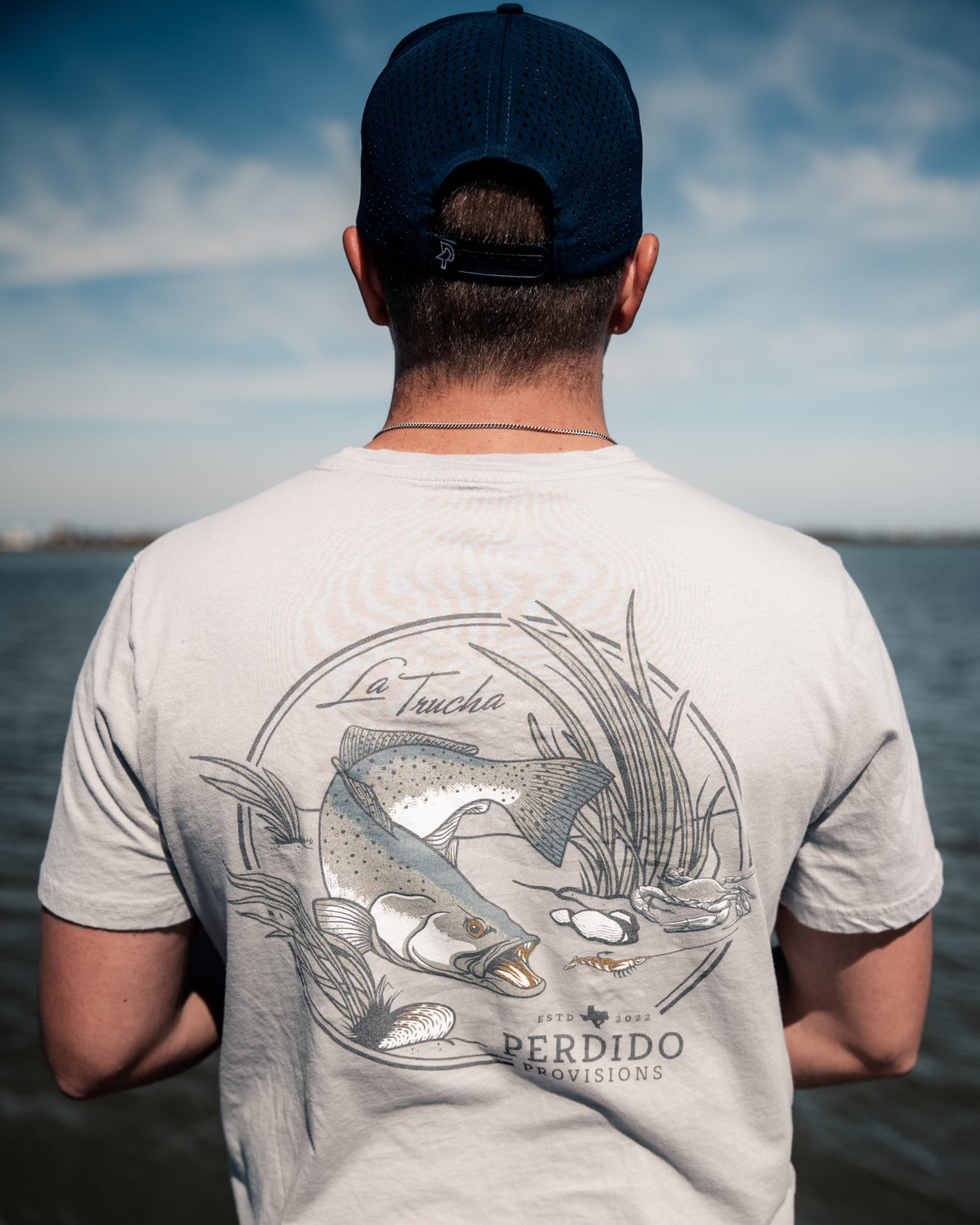 Man wearing La Trucha light grey t-shirt showing the large speckled trout back design outdoors.