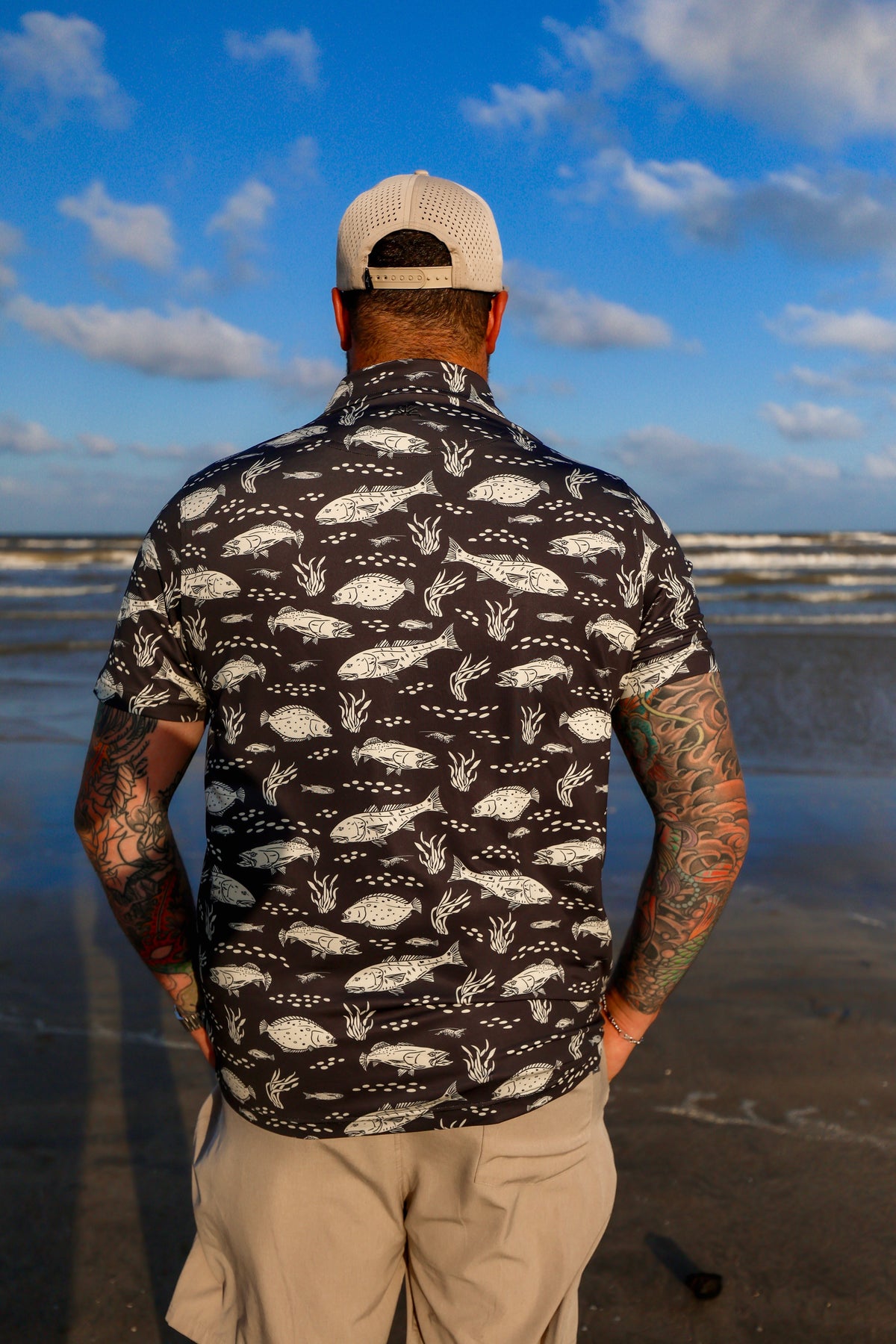 Back view of man on beach wearing black Texas Slam pattern polo.