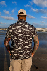 Back view of man on beach wearing black Texas Slam pattern polo.