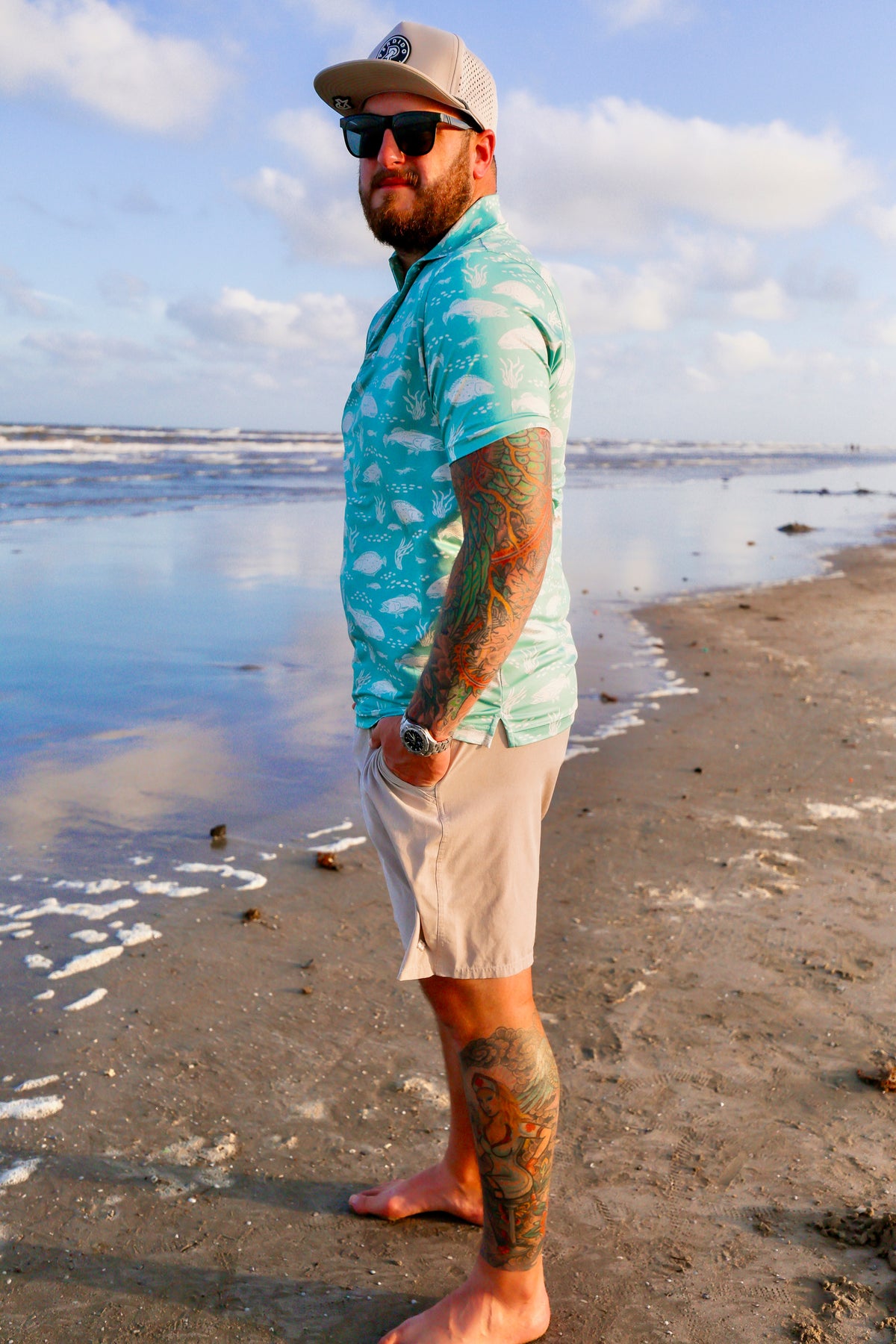 Full-body shot of man on beach wearing light blue Texas Slam polo.